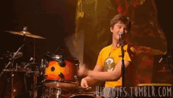 a man in a yellow shirt is playing drums on a stage
