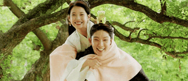 a man is carrying a woman on his back while they are sitting under a tree .
