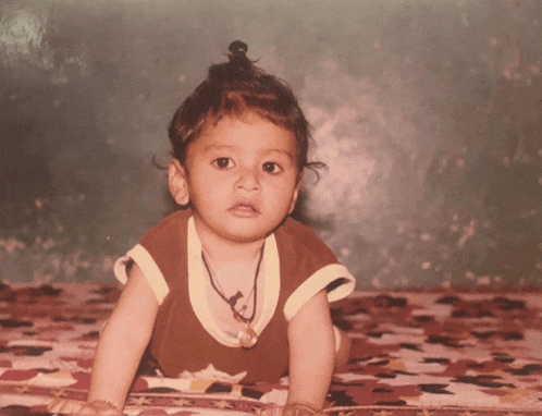 a baby is crawling on a blanket with a necklace around his neck