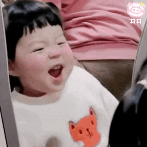 a baby is sitting on a couch with his mouth open and wearing a fox shirt .