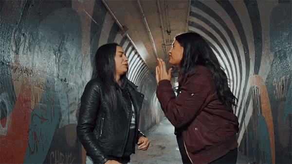 two women are standing next to each other in a tunnel with a striped wall .