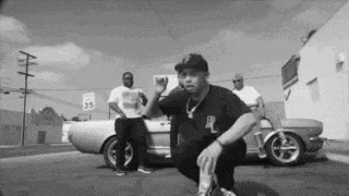 a group of men are squatting in front of a car .