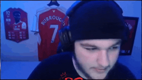 a man wearing headphones and a beanie is sitting in front of a display of jerseys .