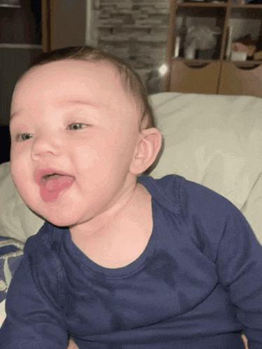 a baby in a blue shirt is sticking out its tongue