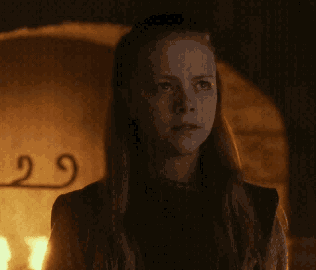 a woman with long hair is standing in front of a fireplace .