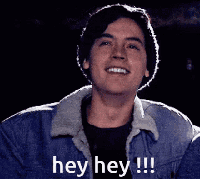 a young man in a denim jacket is smiling and says hey hey !!!
