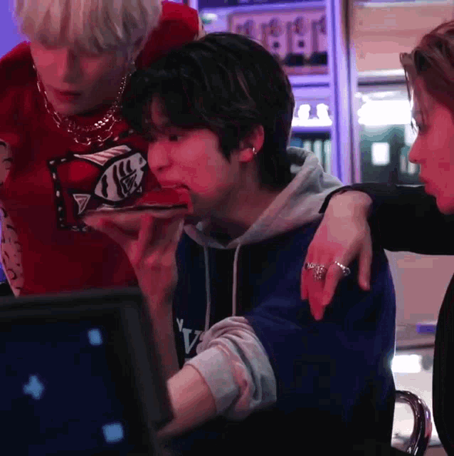 a man in a blue hoodie is eating a piece of pizza while another man looks on .