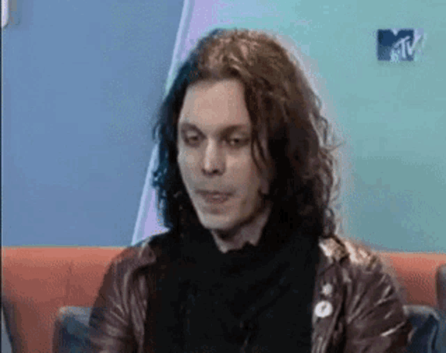 a man with long curly hair is sitting on a couch in front of a tv screen that says mtv