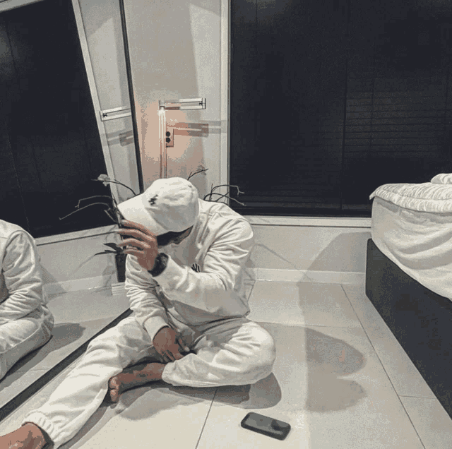 a man sitting on the floor in front of a mirror covering his face with his hands