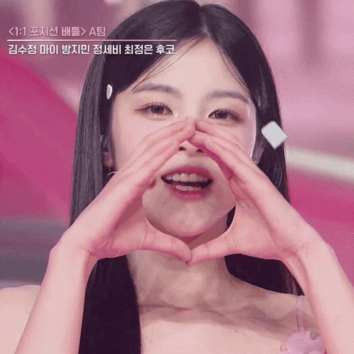 a close up of a woman making a heart shape with her hands with a pink background
