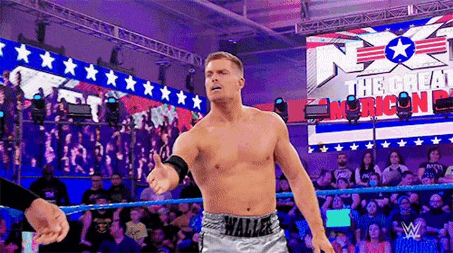 a man without a shirt is standing in a wrestling ring in front of a crowd at a wrestling event .