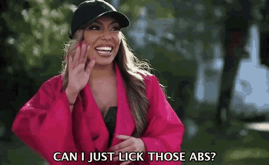 a woman wearing a pink jacket and a black hat says can i just lick those abs ?