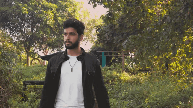 a man wearing a black jacket and a white shirt is standing in a forest