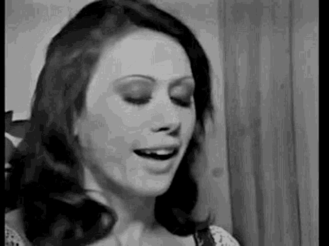 a black and white photo of a woman smiling with her eyes closed .