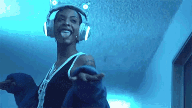 a woman wearing headphones and a cat ear crown is dancing in a dark room .