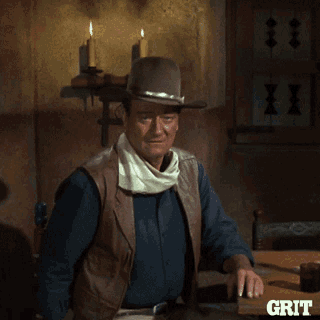 a man wearing a cowboy hat is sitting at a table with the word grit on the bottom