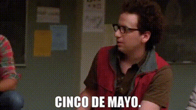 a man in a red vest is talking to another man and the words cinco de mayo are on the screen .