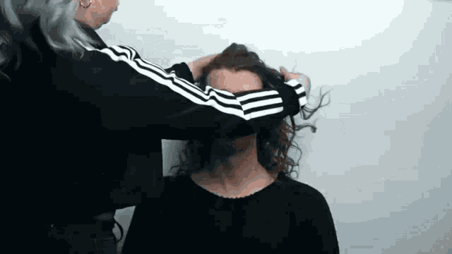 a woman in a black and white adidas jacket is holding a woman 's hair .