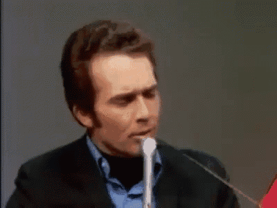 a man is speaking into a microphone while wearing a suit and blue shirt .