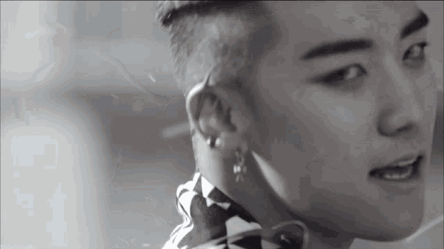 a black and white photo of a young man with a shaved head and earrings