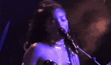 a woman in a purple dress is playing a guitar and singing into a microphone