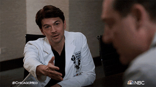 a man in a white lab coat is talking to another man with #chicagomed written on the bottom