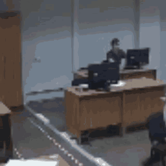 a blurry picture of a man standing in front of a desk with a computer .