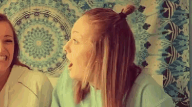 two women are laughing in front of a tapestry with a circular pattern