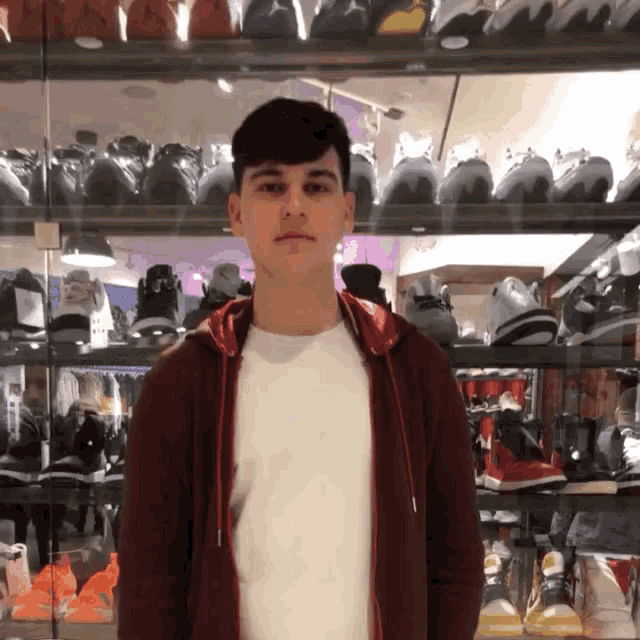 a young man in a red hoodie stands in front of a display of shoes