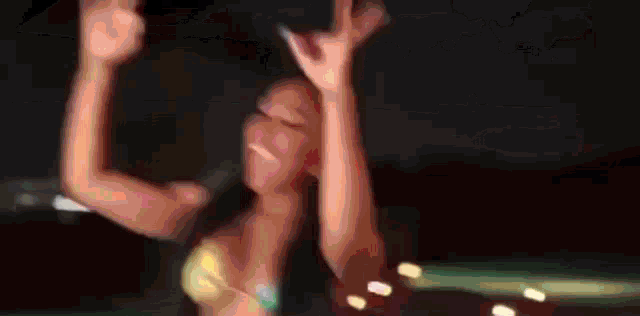 a woman in a bikini is dancing with her arms in the air at night .