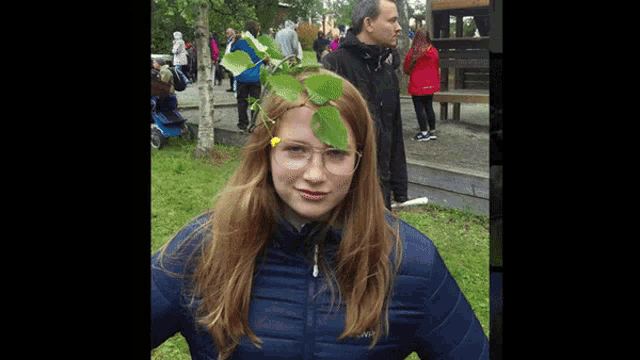 a girl wearing glasses and a blue jacket has a leaf in her hair