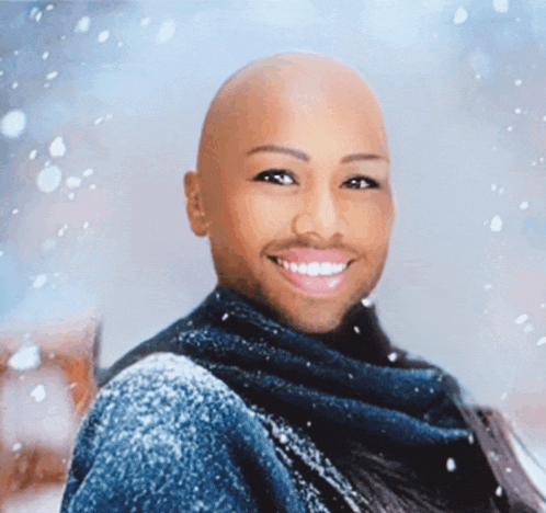 a bald man with a scarf around his neck smiles in front of snow falling