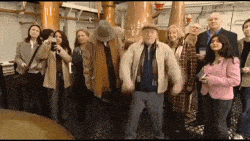 a group of people standing in a room with a man in a hat dancing