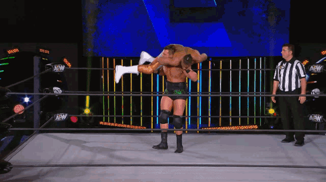 a wrestler is carrying another wrestler on his shoulders in a ring that says aew on the wall