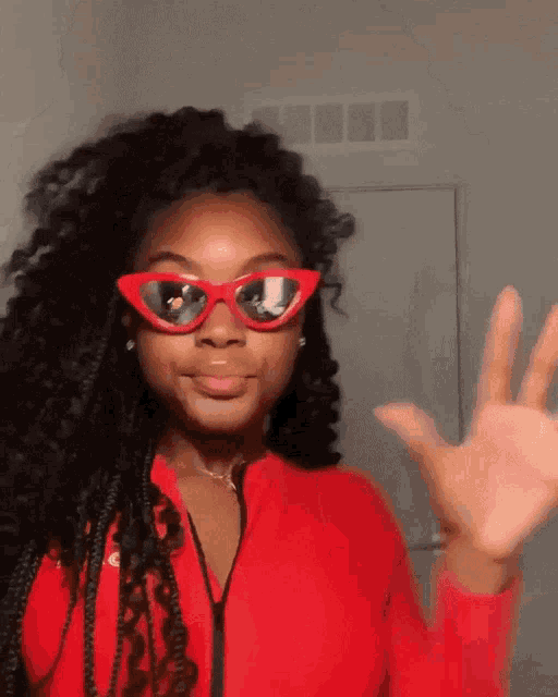 a woman wearing red sunglasses and a red shirt is waving