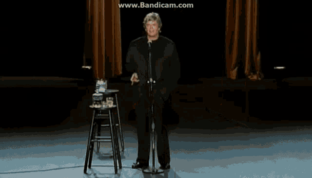 a man stands in front of a microphone on a stage with the website www.bandicam.com in the corner