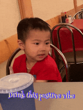 a little boy sits at a table with the words drink this positive vibe written below him