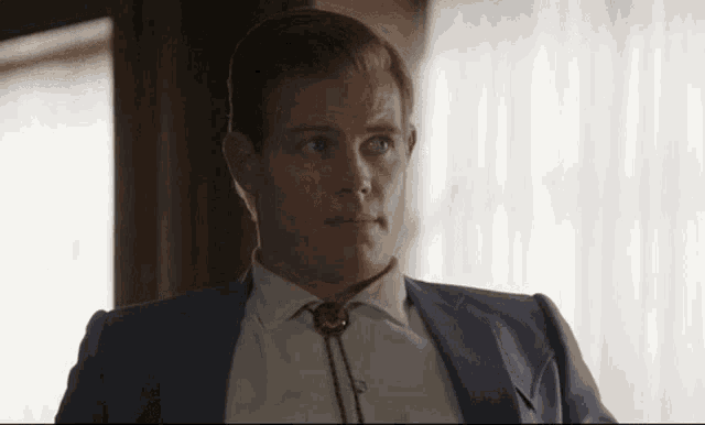 a man wearing a suit and tie with a bolo tie around his neck .
