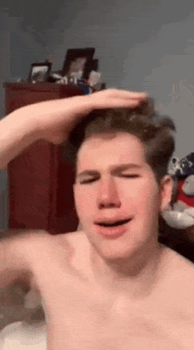 a shirtless man is scratching his head with his hand .