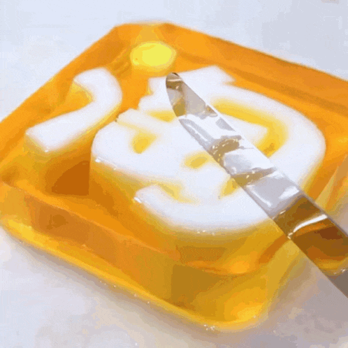 a knife is cutting a piece of yellow soap with the letter e on it