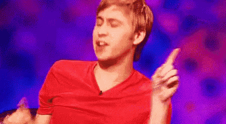 a man in a red shirt is dancing on a stage while pointing up .