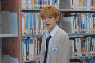 a boy in a school uniform is standing in a library .