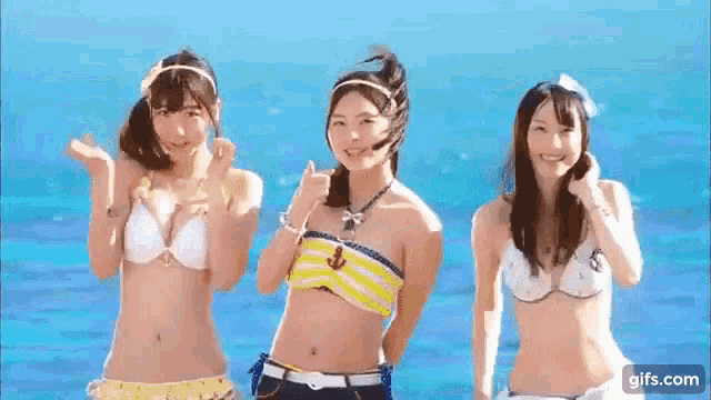 three young women in bikinis are standing next to each other on a beach .