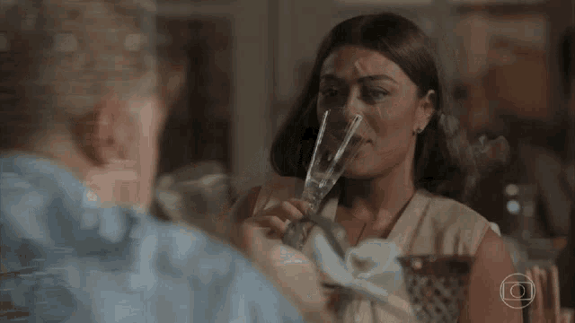 a woman is drinking from a glass while looking at a man .