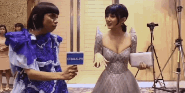 a woman in a blue dress is holding a microphone while talking to another woman in a silver dress .