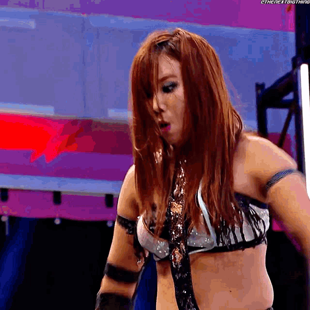 a woman with red hair is standing in a wrestling ring with a purple background .