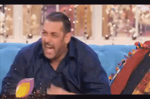 a man is sitting on a blue couch and laughing .