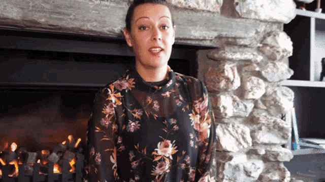 a woman standing in front of a fireplace wearing a floral top