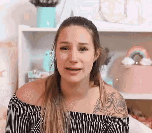 a woman with a tattoo on her arm is crying while sitting in front of a shelf .