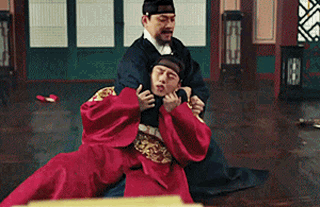 a man in a red robe is being held by another man in a black robe in a room .